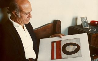 Ο Οδυσσέας Ελύτης στο σπίτι του, το 1980, περιεργάζεται ένα από τα εικαστικά του έργα, για τα οποία επίσης κέρδισε την αγάπη του κοινού. (Αρχείο Ο. Ελύτη / Ι. Ηλιοπούλου)