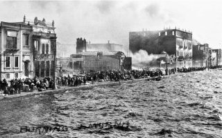 Μετά το πέρασμα της φωτιάς, οι πρόσφυγες επιστρέφουν μπροστά από τα ερείπια των κτιρίων που εξακολουθούν να καπνίζουν. Στο μέσον, ο σκελετός που παραμένει όρθιος ανήκει στο θέατρο «Ιρις» (9.1922).