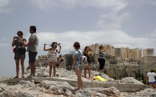 Tourists take photographs as the ancient Acropolis hill is seen in the background in Athens, Monday, July 23, 2018. Greece's foremost tourist attraction, the ancient Acropolis in Athens, is shut to visitors at midday due to forecast high temperatures. (AP Photo/Thanassis Stavrakis)