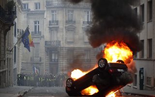 epa07217247 Yellow Vests (Gilets jaunes) protesters are seen behind a burning overturned car near Avenue Marceau during the  demonstration in Paris, France, 08 December 2018. The so-called 'gilets jaunes' (yellow vests) is a protest movement, which reportedly has no political affiliation, that continues protests across the nation over high fuel prices.  EPA/IAN LANGSDON