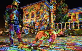 epa08838588 A person with a dog looks at the light projection 'Diving in the sea of colors' by the German light artist Daniel Margraf on the Palais de Rumine in the Place de la Riponne ahead of the Festival Lausanne Lumieres (Lausanne Light Festival), in Lausanne, Switzerland, 23 November 2020 (issued 24 November 2020). Eight projections on different buildings aiming to showcase the city of Lausanne under a new light will be on shows during the festival that runs from 24 November to 24 December 2020.  EPA/LAURENT GILLIERON