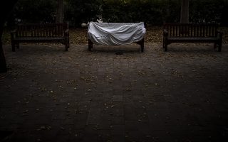 A homeless man covered by a sheet sleeps on a bench at a public park in Barcelona, Spain, Sunday, Dec. 20, 2020. (AP Photo/Emilio Morenatti)